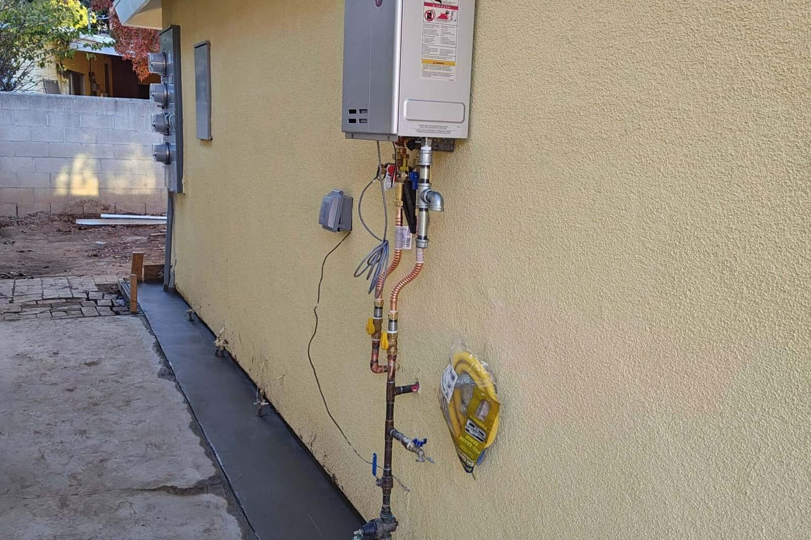 Gas line installation on the exterior wall of a house with yellow stucco, demonstrating expert plumbing and energy solutions by Andromeda Construction Inc.